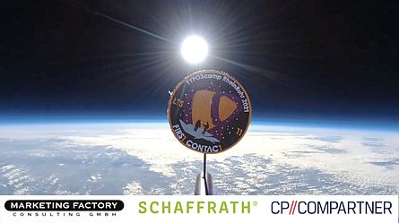 A mission patch in the stratosphere. The Earth's cloud cover and the sun can be seen in the background.